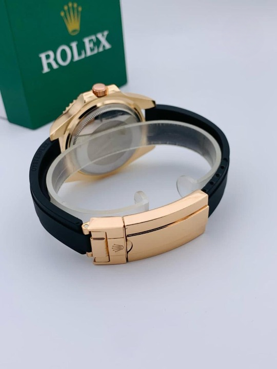 Men's luxury gold watch back view showing gold deployant clasp on black rubber strap with green gift box