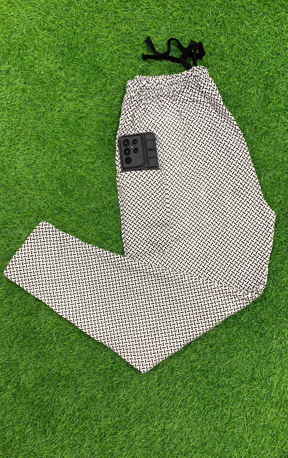 Men's geometric print drawstring trousers folded on green grass with phone in pocket – flat lay shot