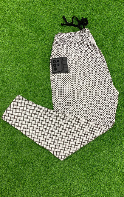 Men's geometric print drawstring trousers folded on green grass with phone in pocket – flat lay shot