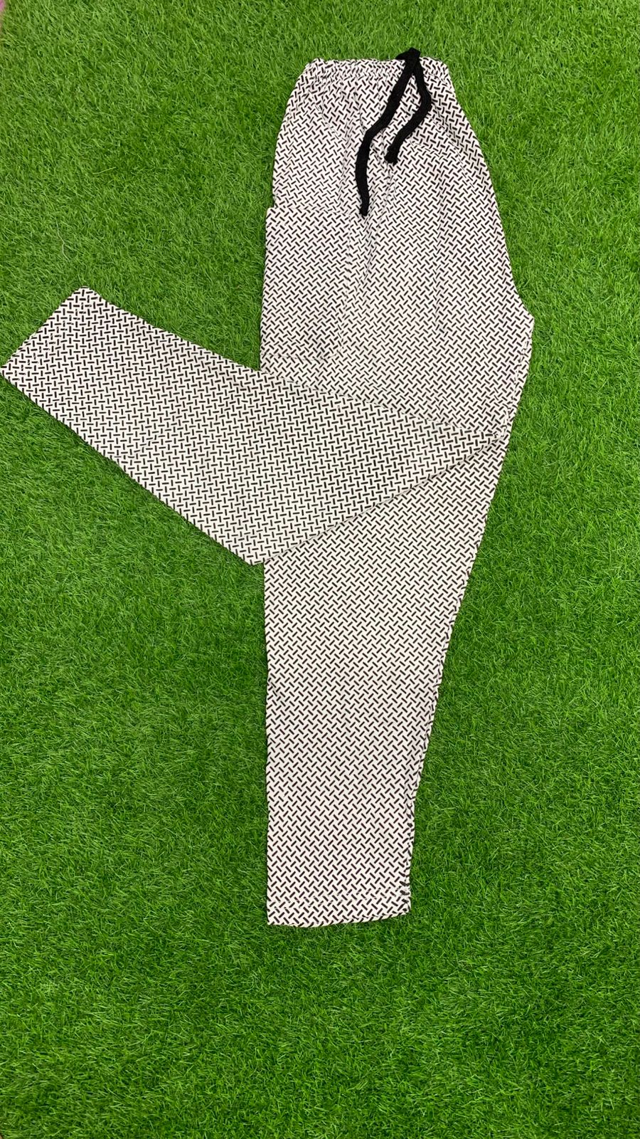 Men's geometric print drawstring trousers laid flat on green grass – full length product shot