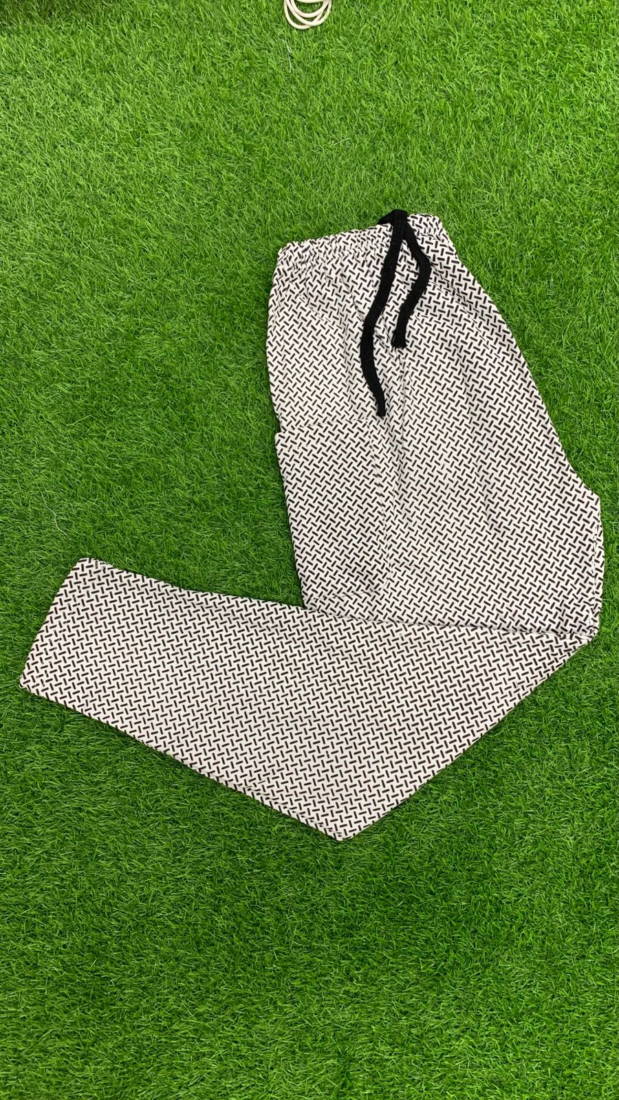 Men's geometric print drawstring trousers folded on green grass – top view flat lay