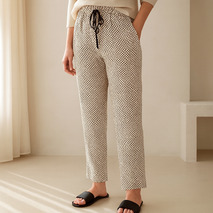 Woman wearing geometric print drawstring trousers with white top and black sandals – lifestyle model shot in minimal room