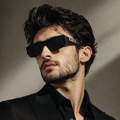 Man wearing black rectangular sunglasses with gold leopard logo – front lifestyle shot in natural light