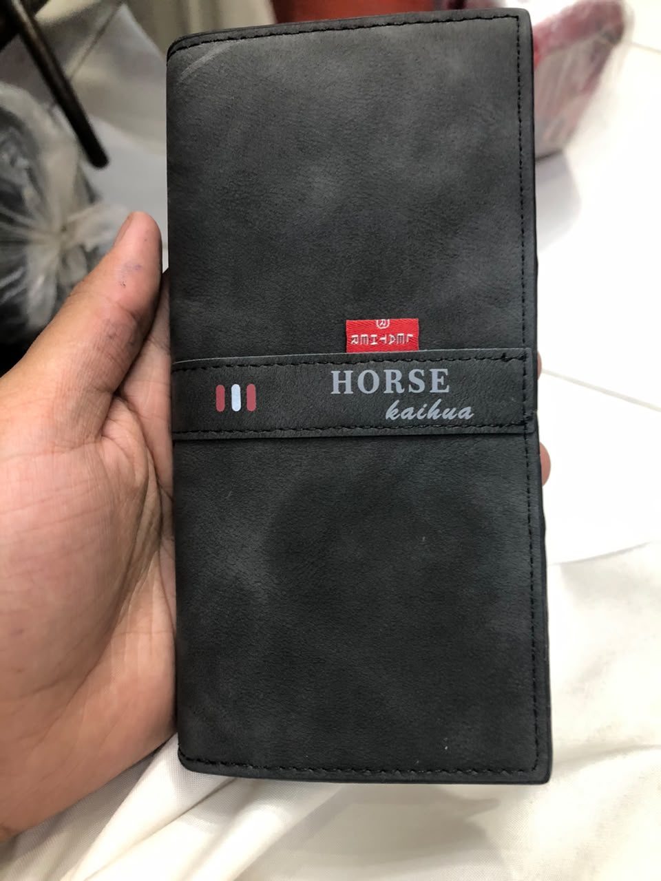 Horse Kaihua long leather wallet in Black held in hand showing front distressed leather texture and branded strap detail