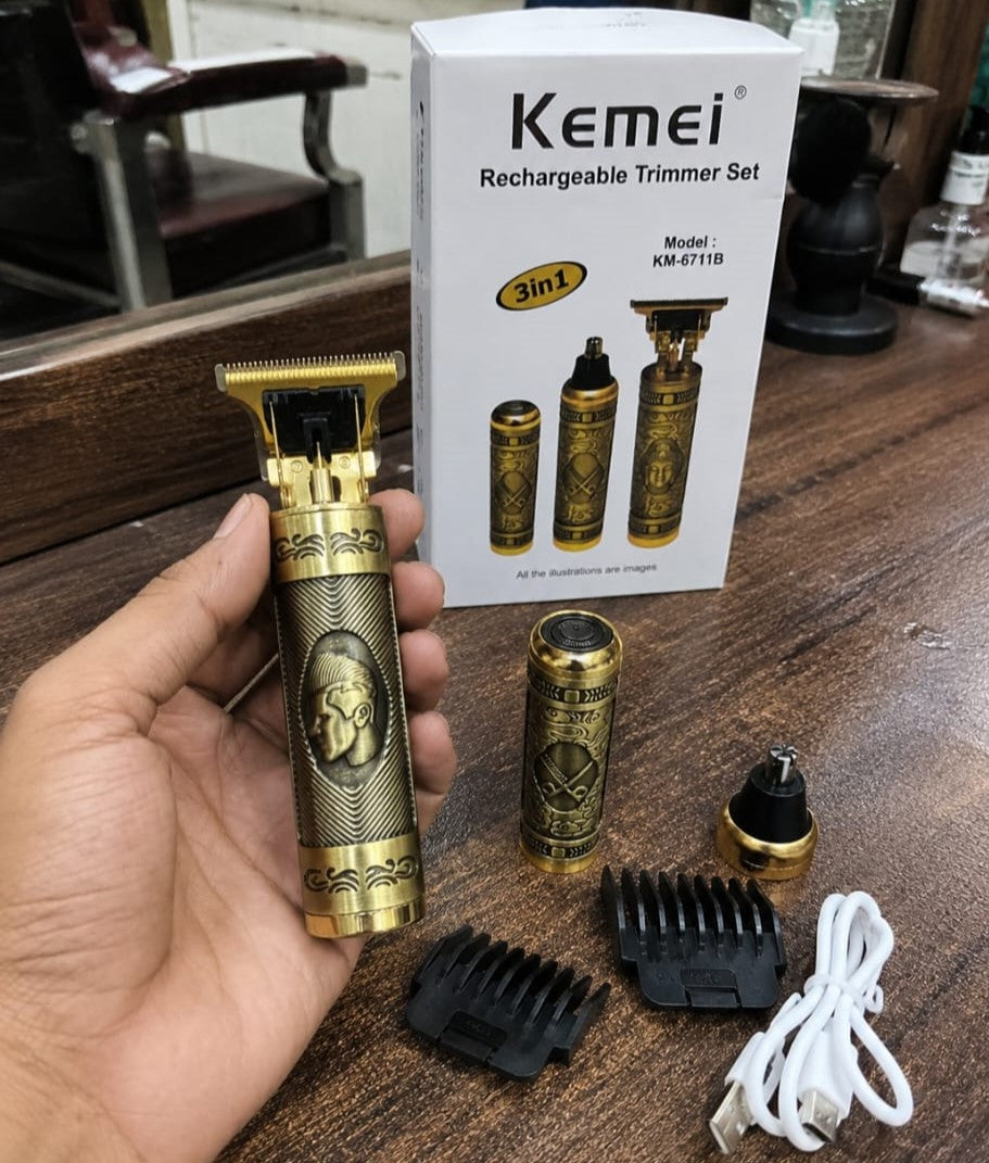 Kemei KM-6711B hair beard trimmer held in hand showing gold engraved antique design with box guide combs nose trimmer attachment and USB cable on wooden barbershop table