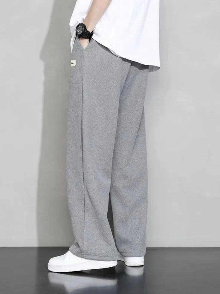 Man wearing grey premium micro plain trouser with white t-shirt and white sneakers – side view lifestyle shot on grey background