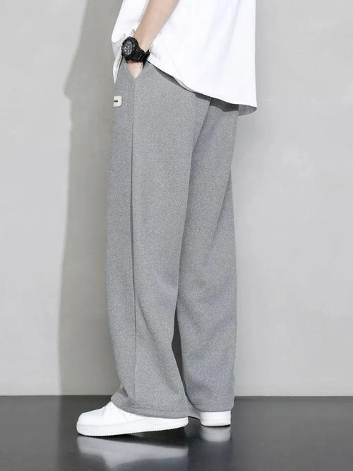 Man wearing grey premium micro plain trouser with white t-shirt and white sneakers – side view lifestyle shot on grey background