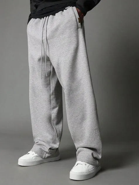 Man wearing grey premium micro plain trouser with black hoodie and white sneakers – front view lifestyle shot on grey background