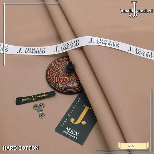 Junaid Jamshed Hard Cotton unstitched fabric in Rust color folded on dark wooden surface with gold pins and J. Men brand tag