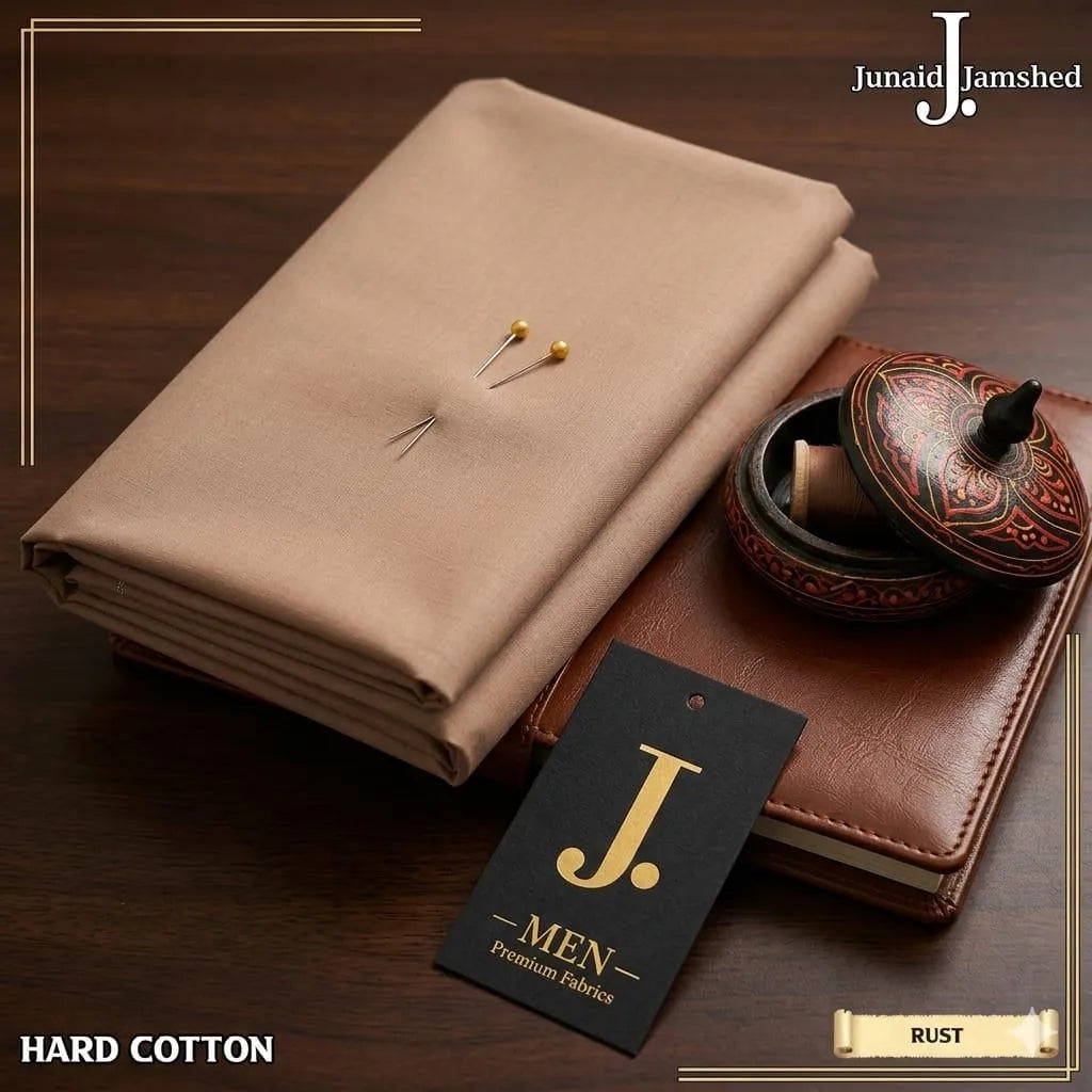 Junaid Jamshed Hard Cotton unstitched fabric in Rust color layered on leather journal with J. Men premium fabrics tag