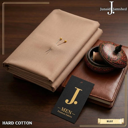 Junaid Jamshed Hard Cotton unstitched fabric in Rust color layered on leather journal with J. Men premium fabrics tag