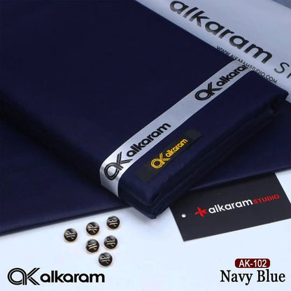 Alkaram Studio AK-102 Navy Blue unstitched cotton fabric folded with branded ribbon buttons and Alkaram Studio brand tag on white background