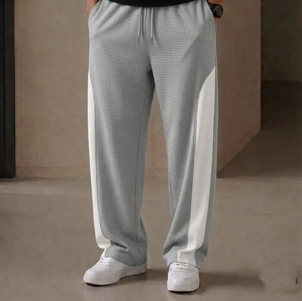 Man wearing grey waffle knit white side panel drawstring trousers with black t-shirt and white sneakers – close up front view on beige background
