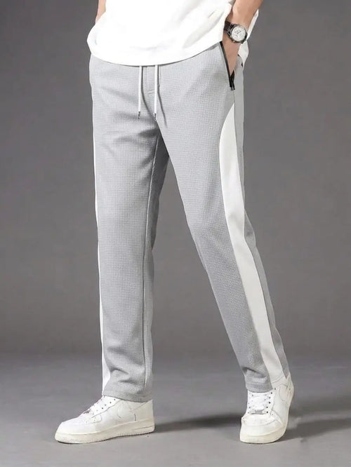 Man wearing grey waffle knit white side panel drawstring trousers with white t-shirt and white sneakers – full body side view on grey background