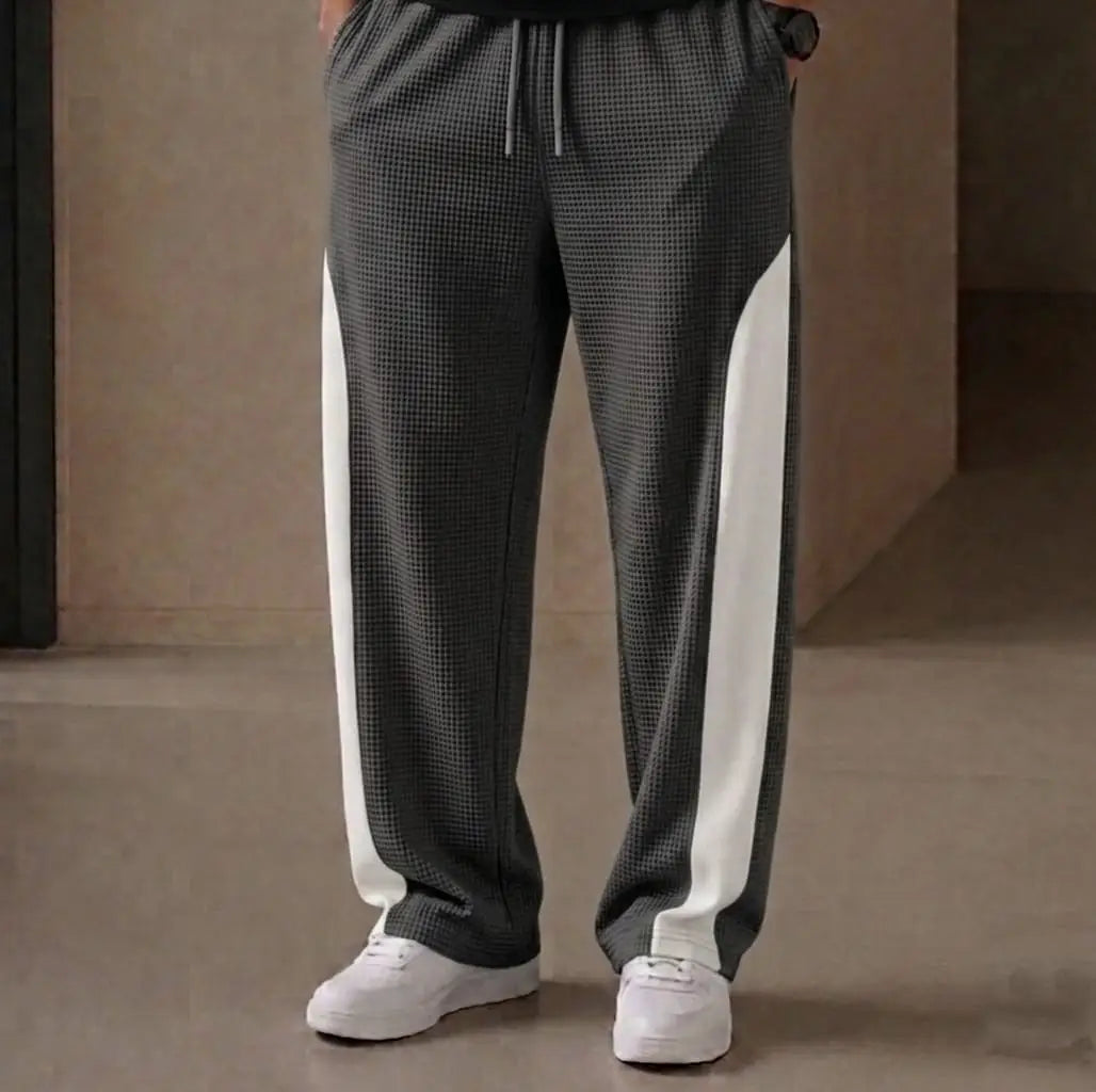 Man wearing grey waffle knit side stripe drawstring trousers with white sneakers – close up front view