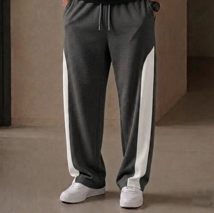 Man wearing grey waffle knit side stripe drawstring trousers with white sneakers – close up front view