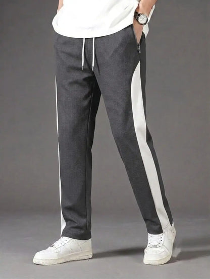Man wearing grey waffle knit side stripe drawstring trousers with white t-shirt and white sneakers – full body model shot on grey background