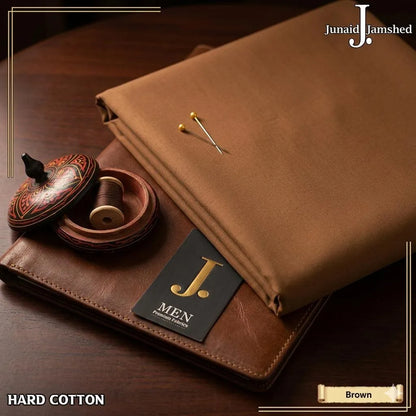 Junaid Jamshed Hard Cotton unstitched fabric in Copper color folded on dark wooden surface with gold pins and J. Men brand tag