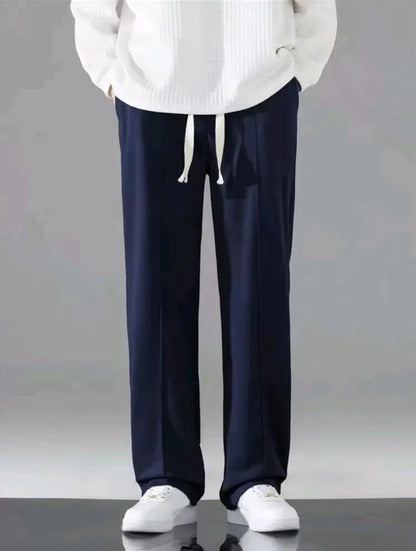 Man wearing navy blue dri-fit drawstring trousers with white hoodie and white sneakers – front model shot on grey background